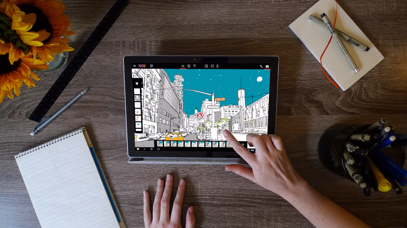 Shows a desktop with a Microsoft surface tablet running Mental Canvas software.  The pictures shows a woman's hand touching the screen and several desk items around the tablet.